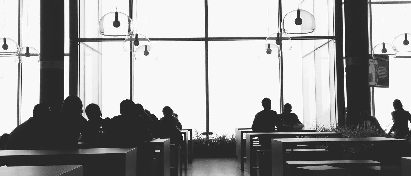 Menschen im Gespräch an Cafétischen vor einem großen Fenster