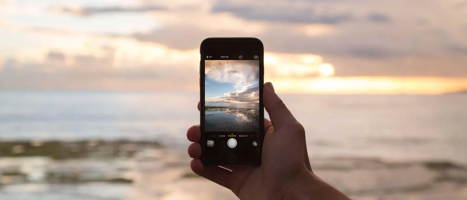 Hand hält ein Smartphone und fotografiert das Meer